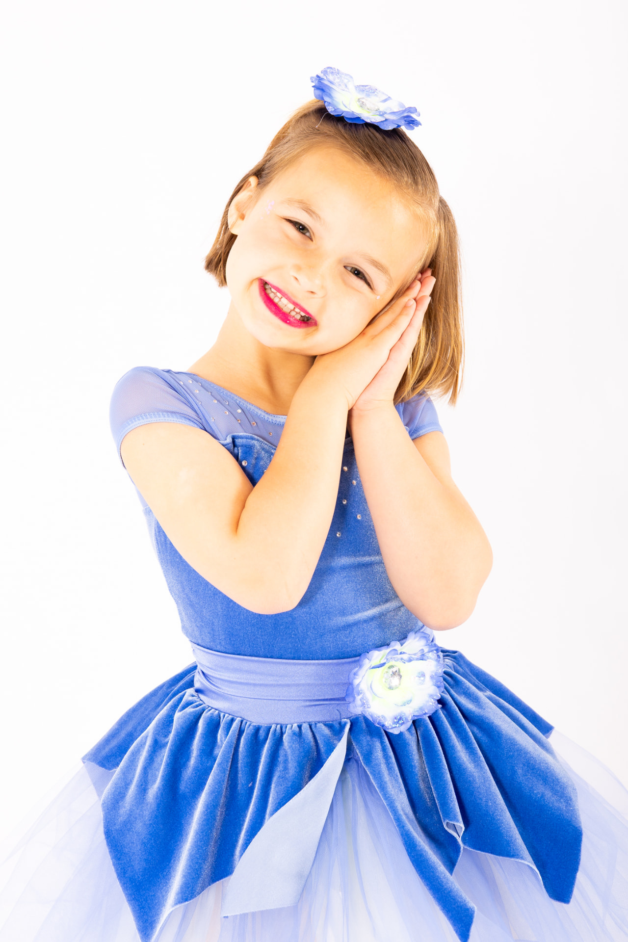 A Kinderdance student in a blue costume resting her cheek on her hands