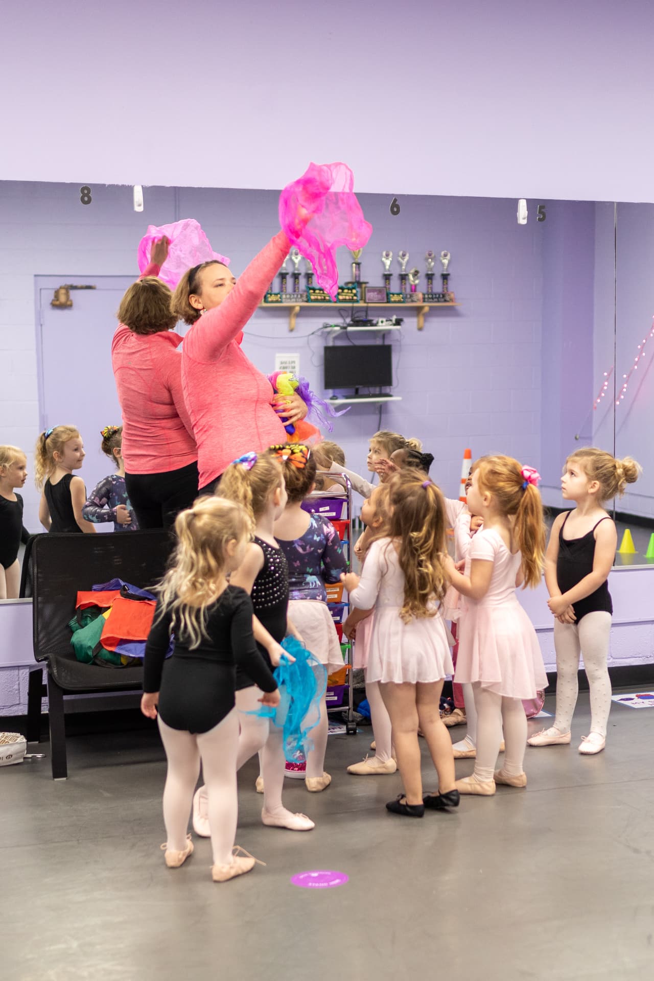 A Music in Motion teacher holding up pink scarves for a circle of preschool dancers