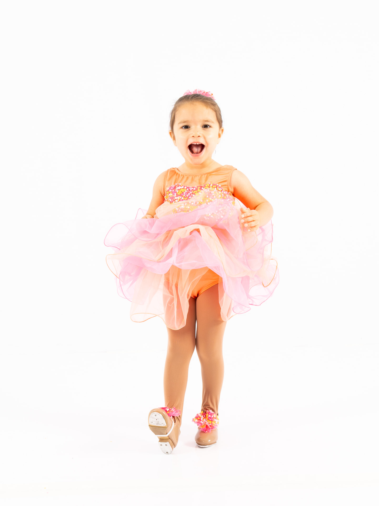 A young tap dancer laughing in a peach sequined costume