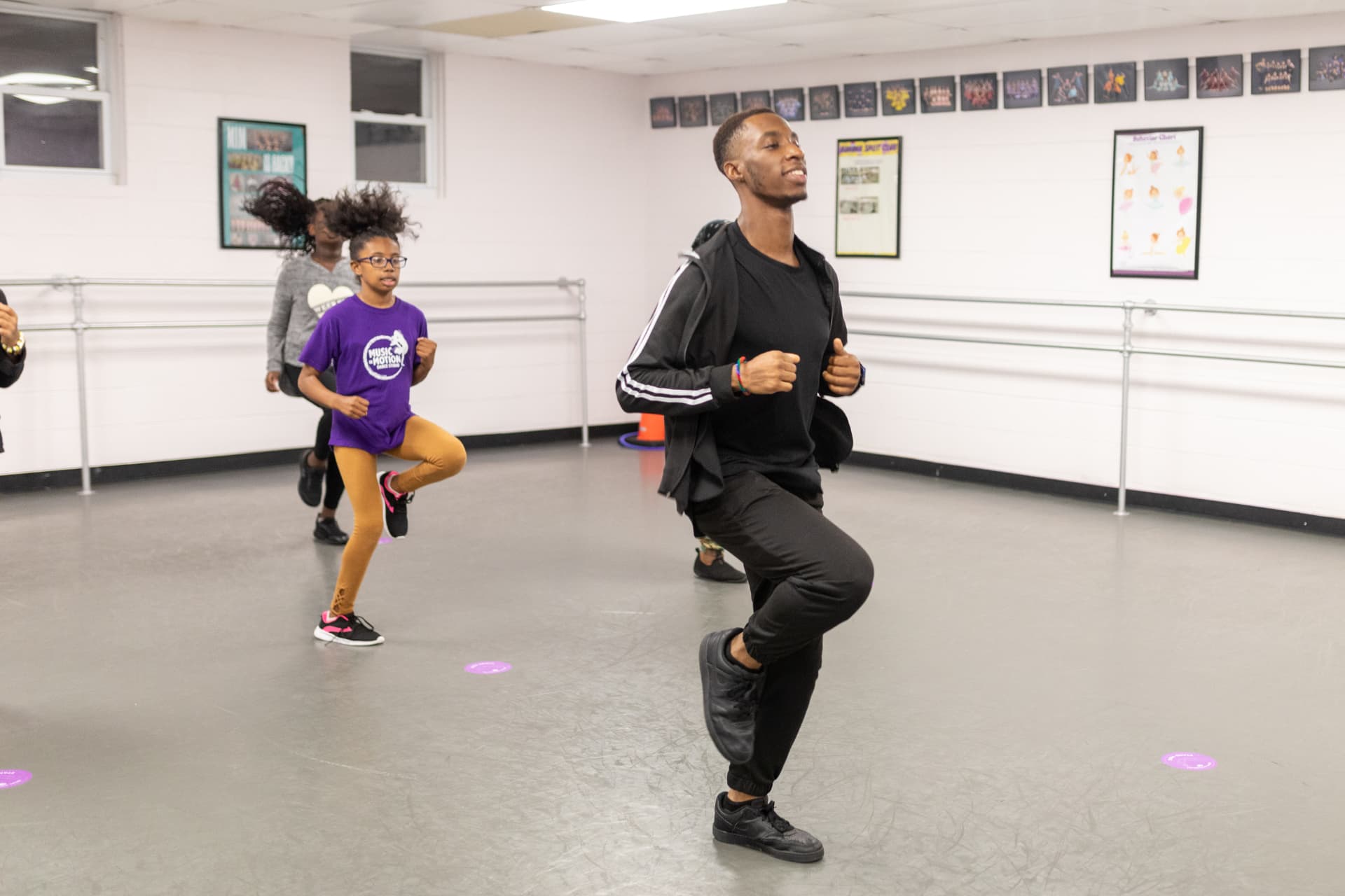 A Music in Motion teacher leading young dancers in a hip hop warm up across the studio floor