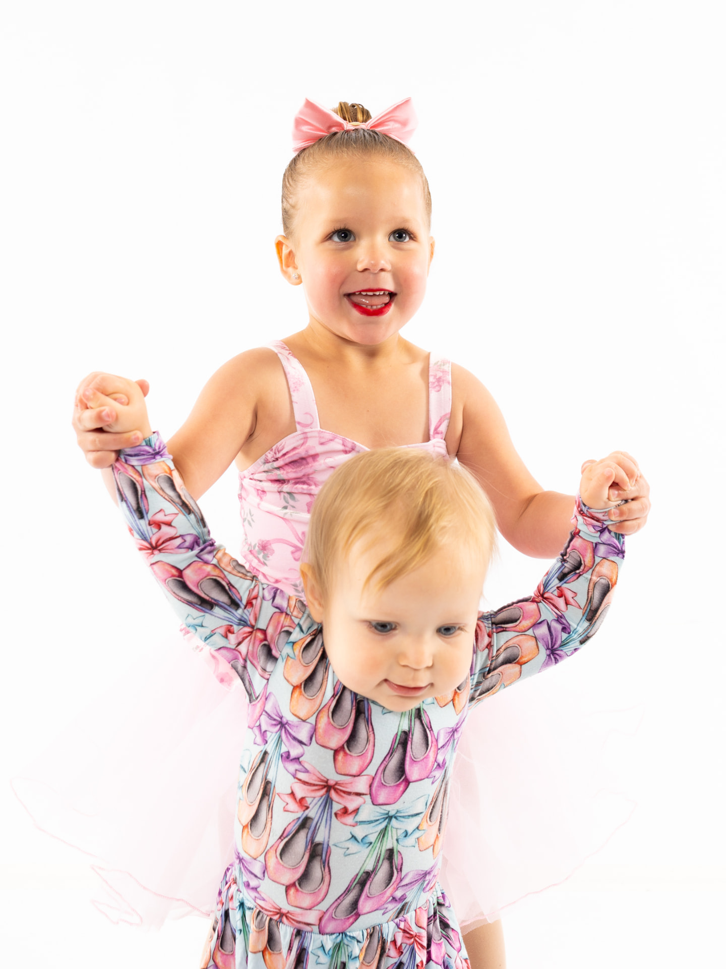 An older dancer holding a toddler's hands while both wear ballet tutus