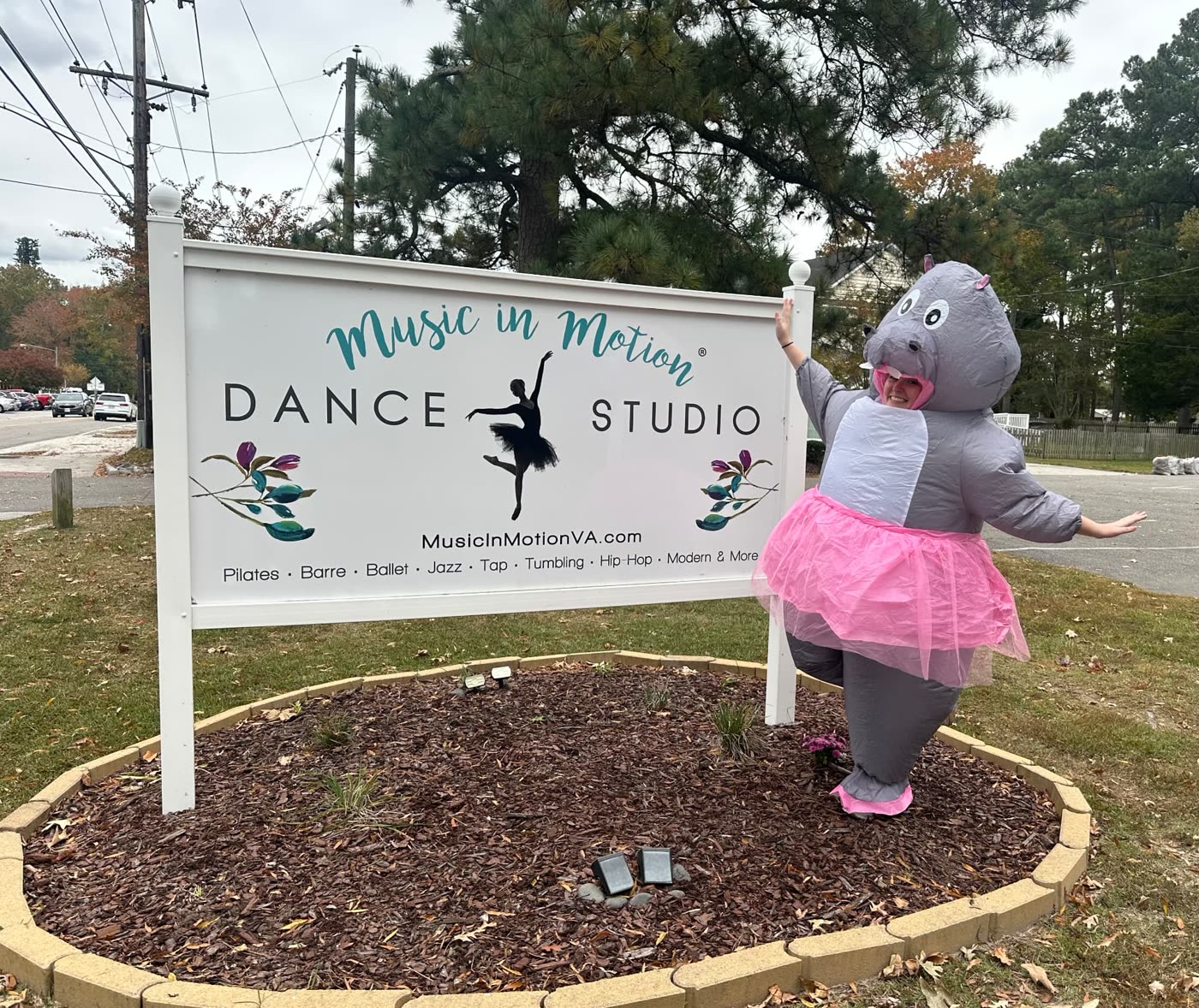 A Music in Motion teacher in an inflatable hippo costume and pink tutu posing by the studio sign
