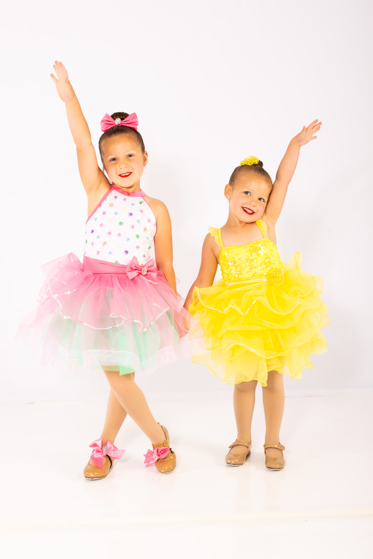 Two young tap dancers in tutus reaching one arm to the sky
