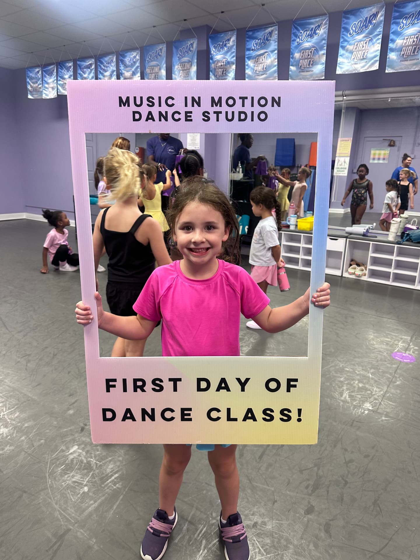 A smiling dancer holding the First Day of Dance Class photo frame in the studio