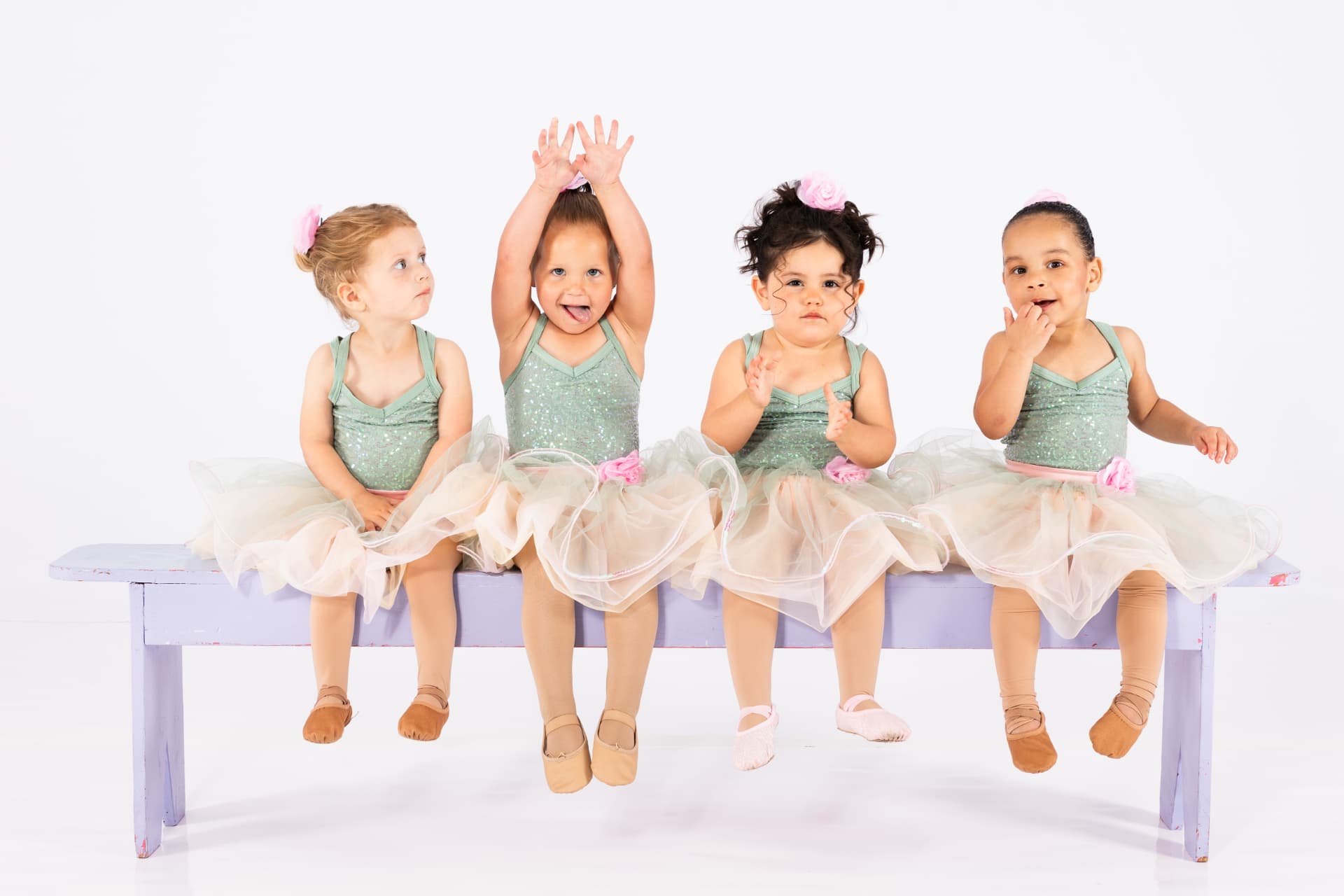 Four toddler dancers in tutus sitting together on a bench in the studio