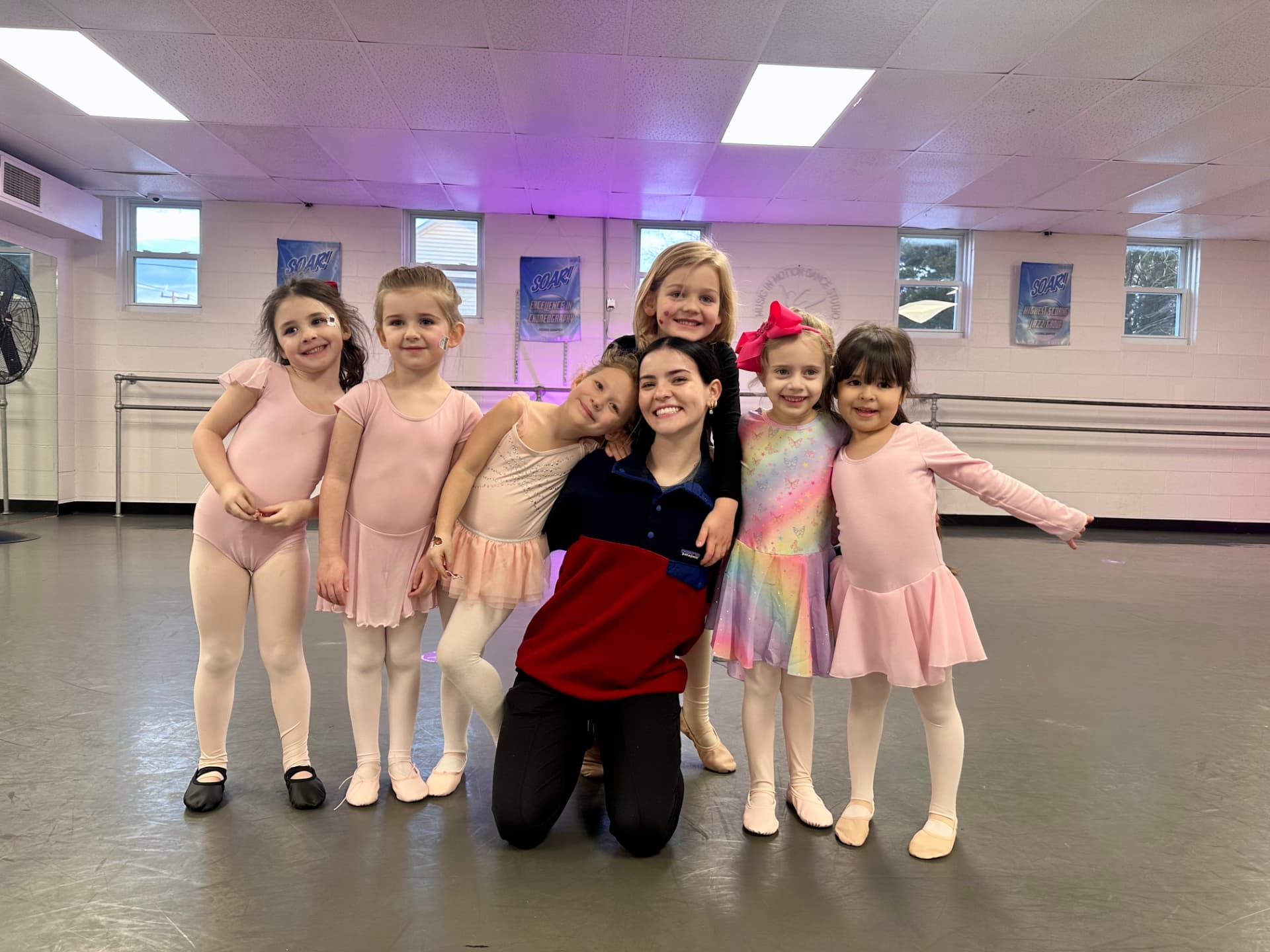 A preschool dance class hugging their teacher in the studio