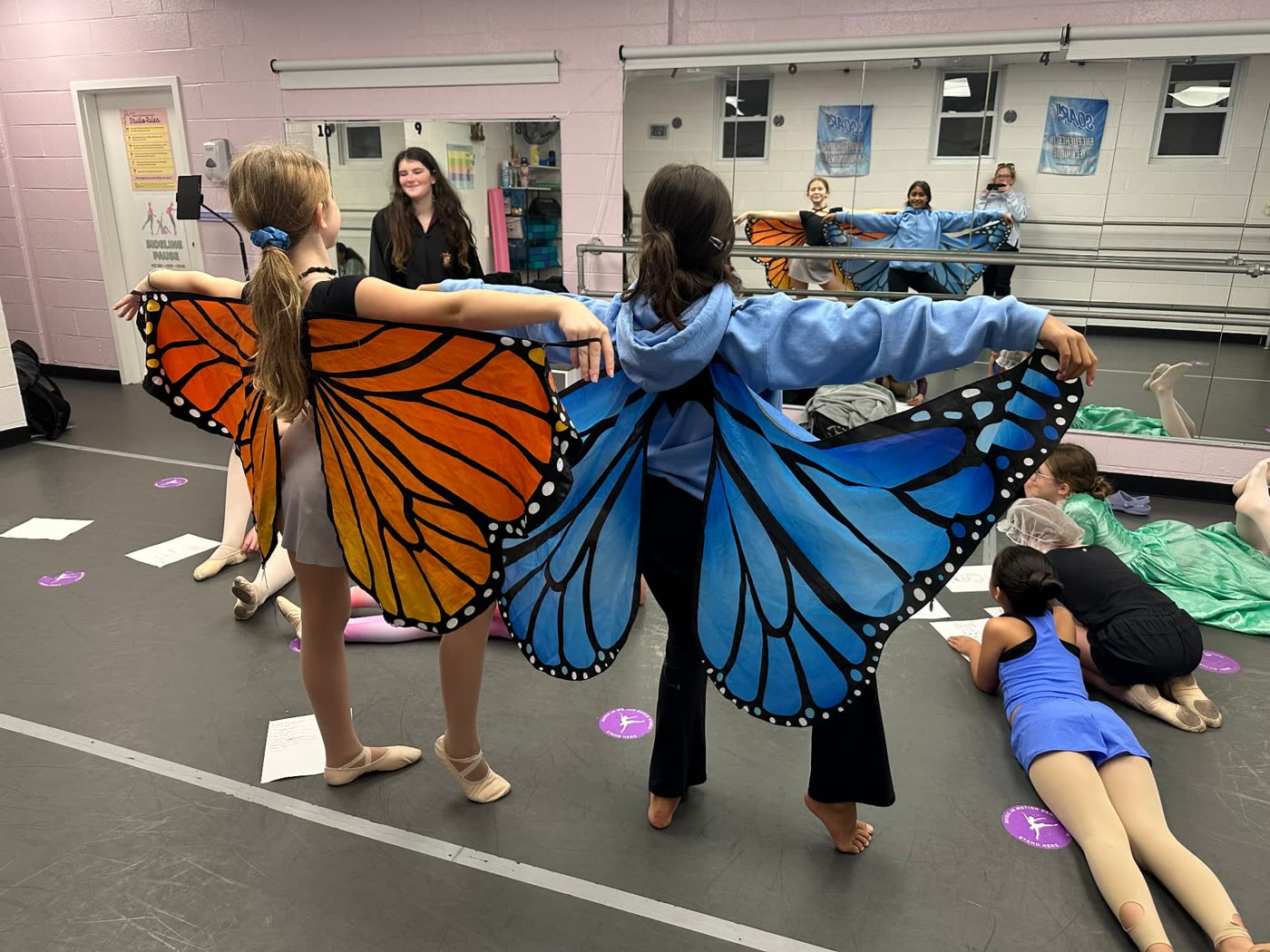 Two dancers spreading orange and blue butterfly wings in the studio during Halloweek
